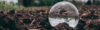 Une sphère cristalline reflétant la nature, posée sur de la terre fertile, illustrant l’engagement de Green Horiz’Home pour préserver l’environnement à chaque étape de ses services.